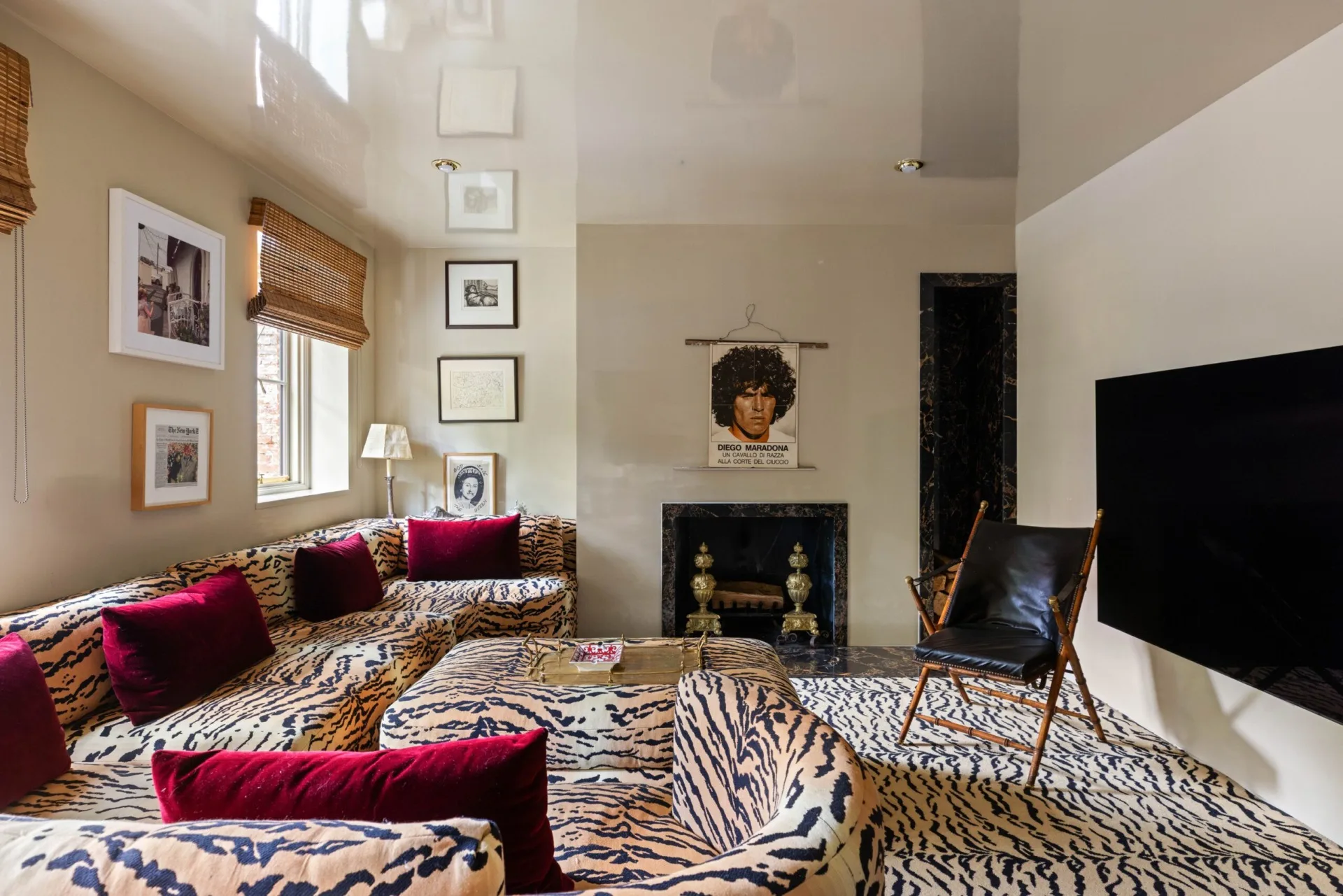 Living room with tiger-print carpet, sofa and ottoman. Red cushions, framed art, and a fireplace are elsewhere in the space.