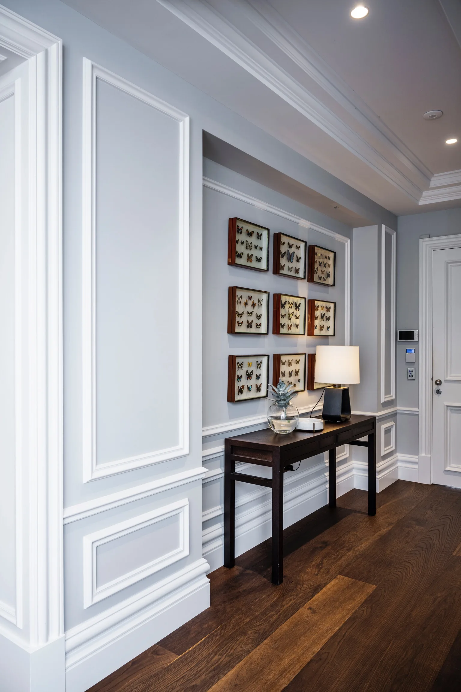 Nicole Gazal O'Neil's hallway table and antique framed butterflies, with wainscoting and timber floorboards.