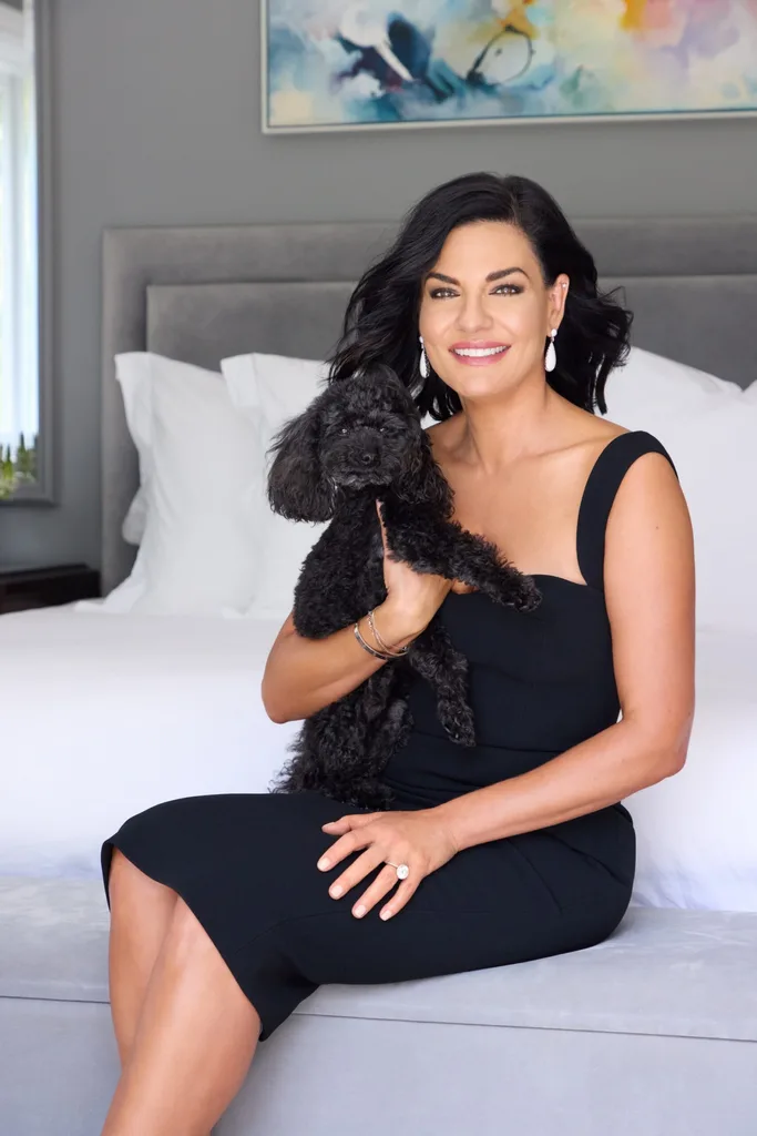 Portait of Nicole Gazal O'Neil in her bedroom wearing a black dress and holding her dog.