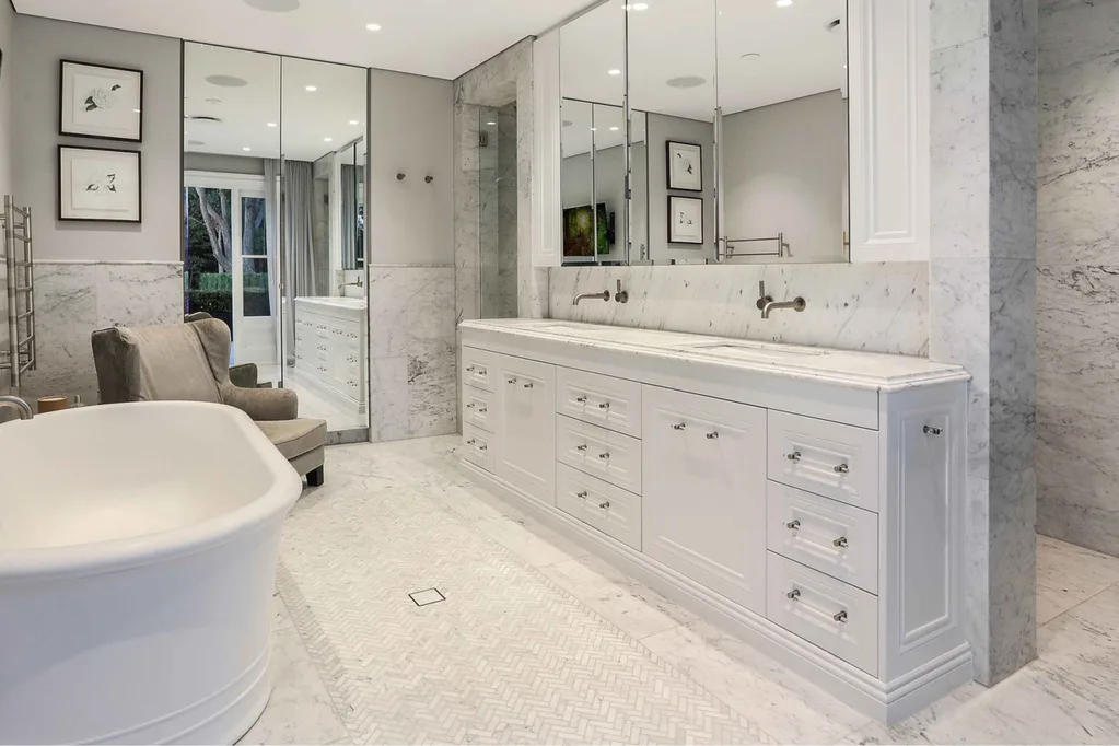 Nicole Gazal O’Neil’s white and grey marble bathroom, featuring a bathtub, herringbone-tiled floor and mirrored cabinet.