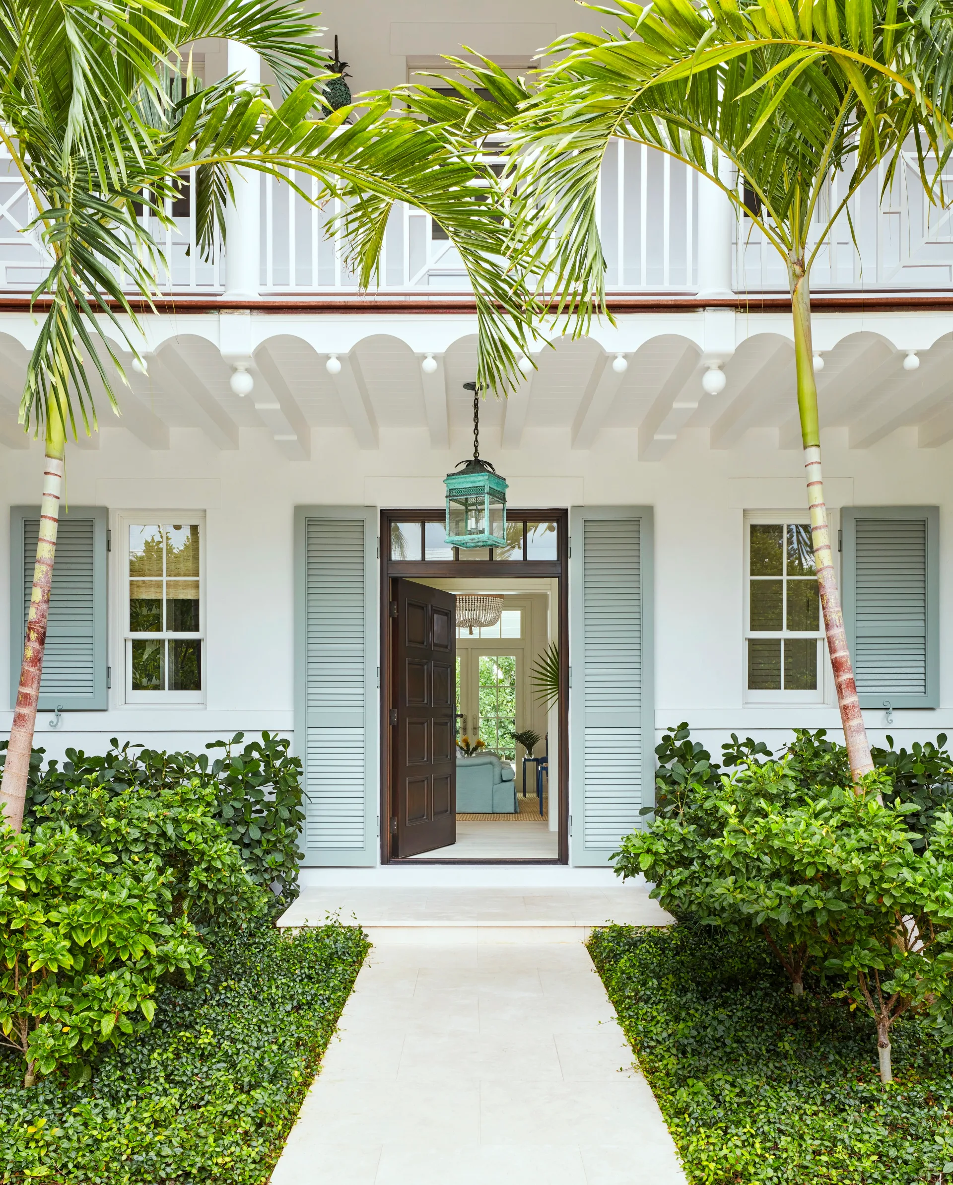 Entrance of a tropical-style house with open double doors, flanked by palm trees and lush greenery.