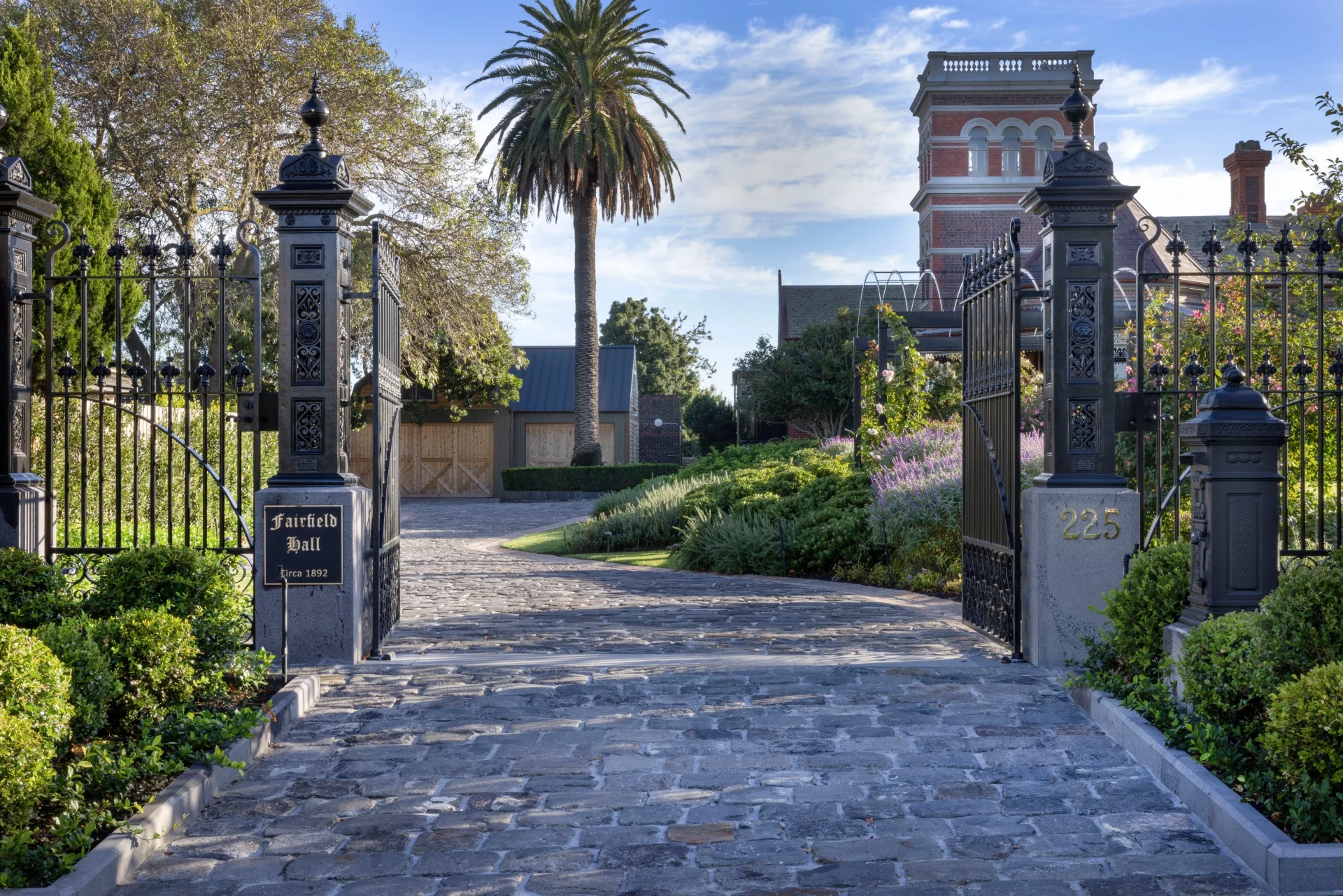 Grand entrance gate to Fairfield Hall, built circa 1892, with landscaped gardens and a historic building visible. The garden was designed by iconic Australian garden designer Paul Bangay.