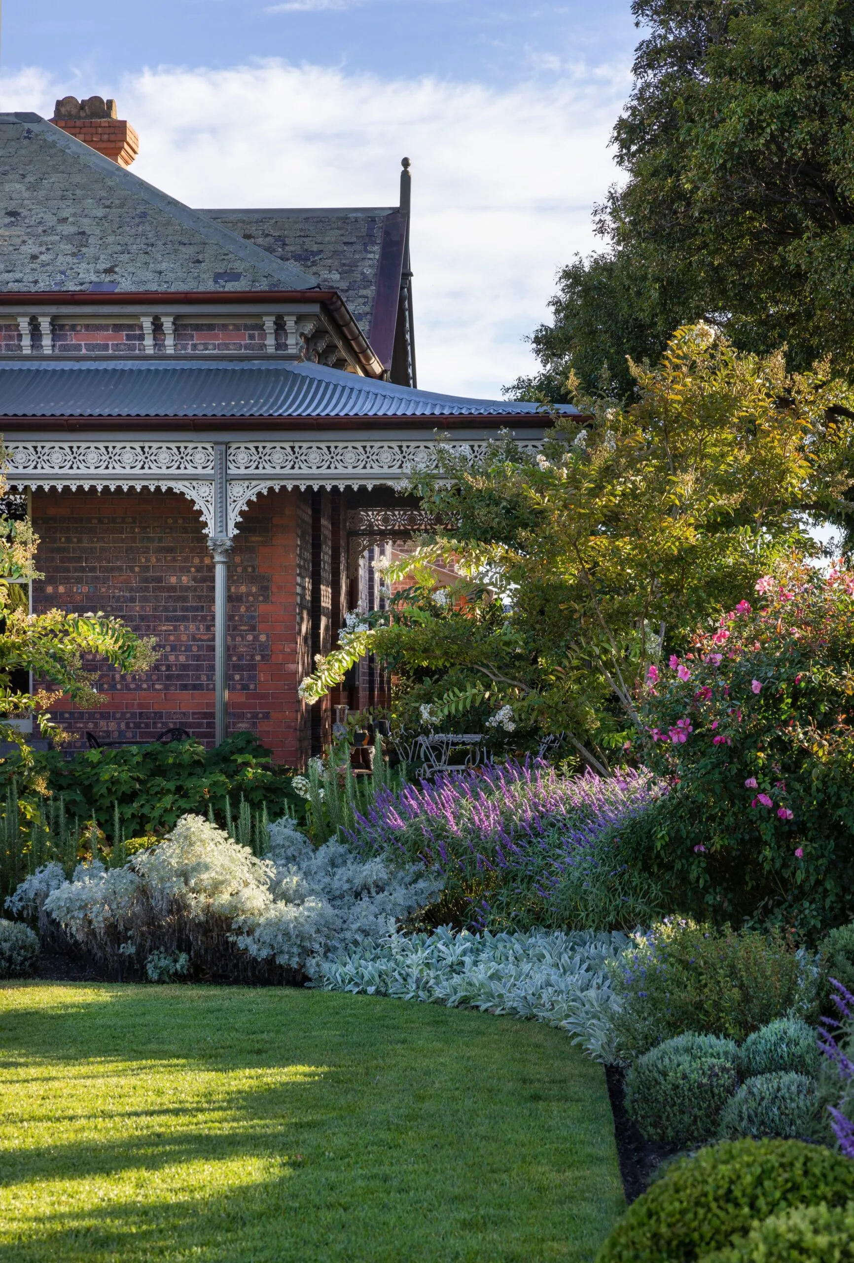 Victorian house with ornate veranda, lush garden with purple flowers, green shrubs, and a manicured lawn. The garden was designed by iconic Australian garden designer Paul Bangay.