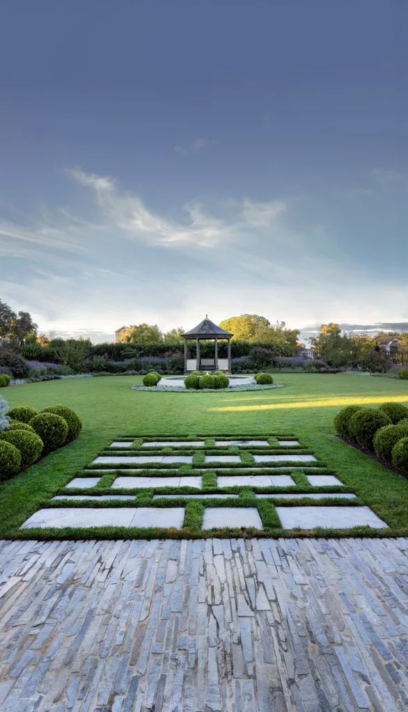 A garden with a stone pathway leading to a gazebo under a clear blue sky. The garden was designed by iconic Australian garden designer Paul Bangay.