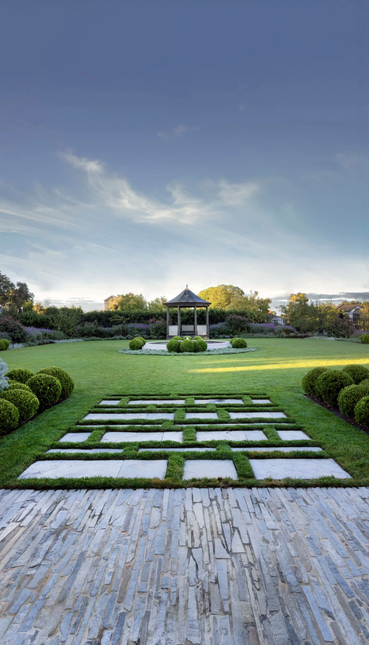 A garden with a stone pathway leading to a gazebo under a clear blue sky. The garden was designed by iconic Australian garden designer Paul Bangay.