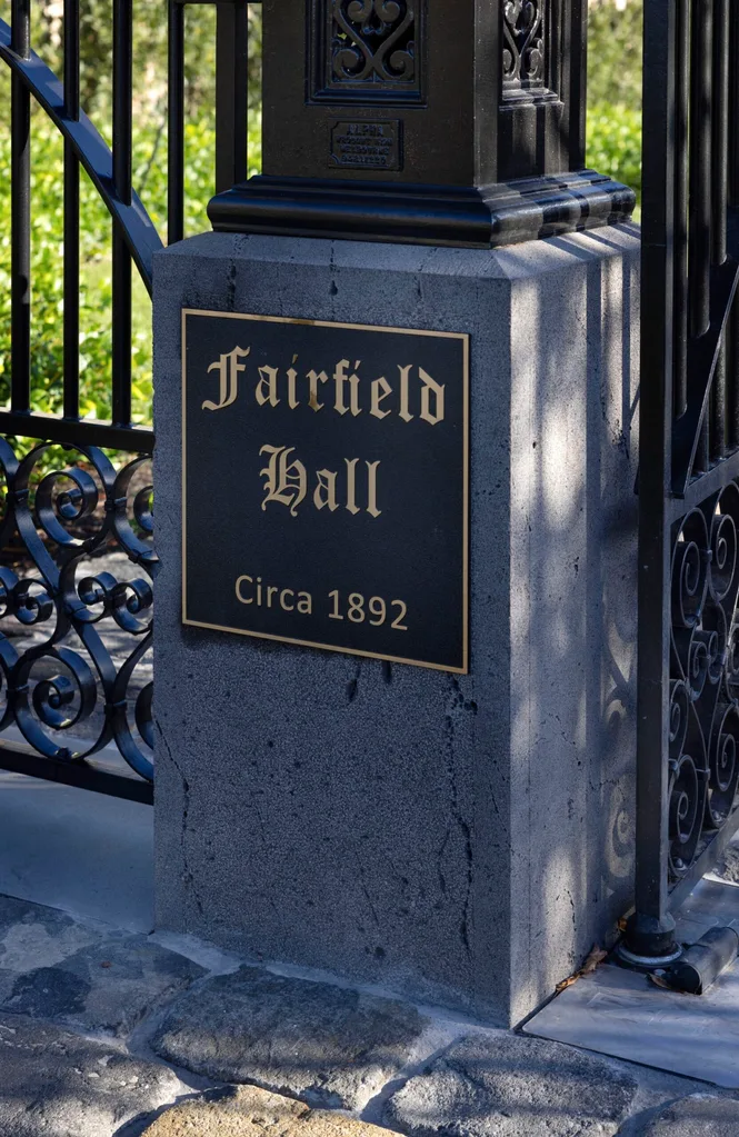 A close up of the pillar of a stone and wrought iron gate, with a sign that read "Fairfield Hall, circa 1892'
