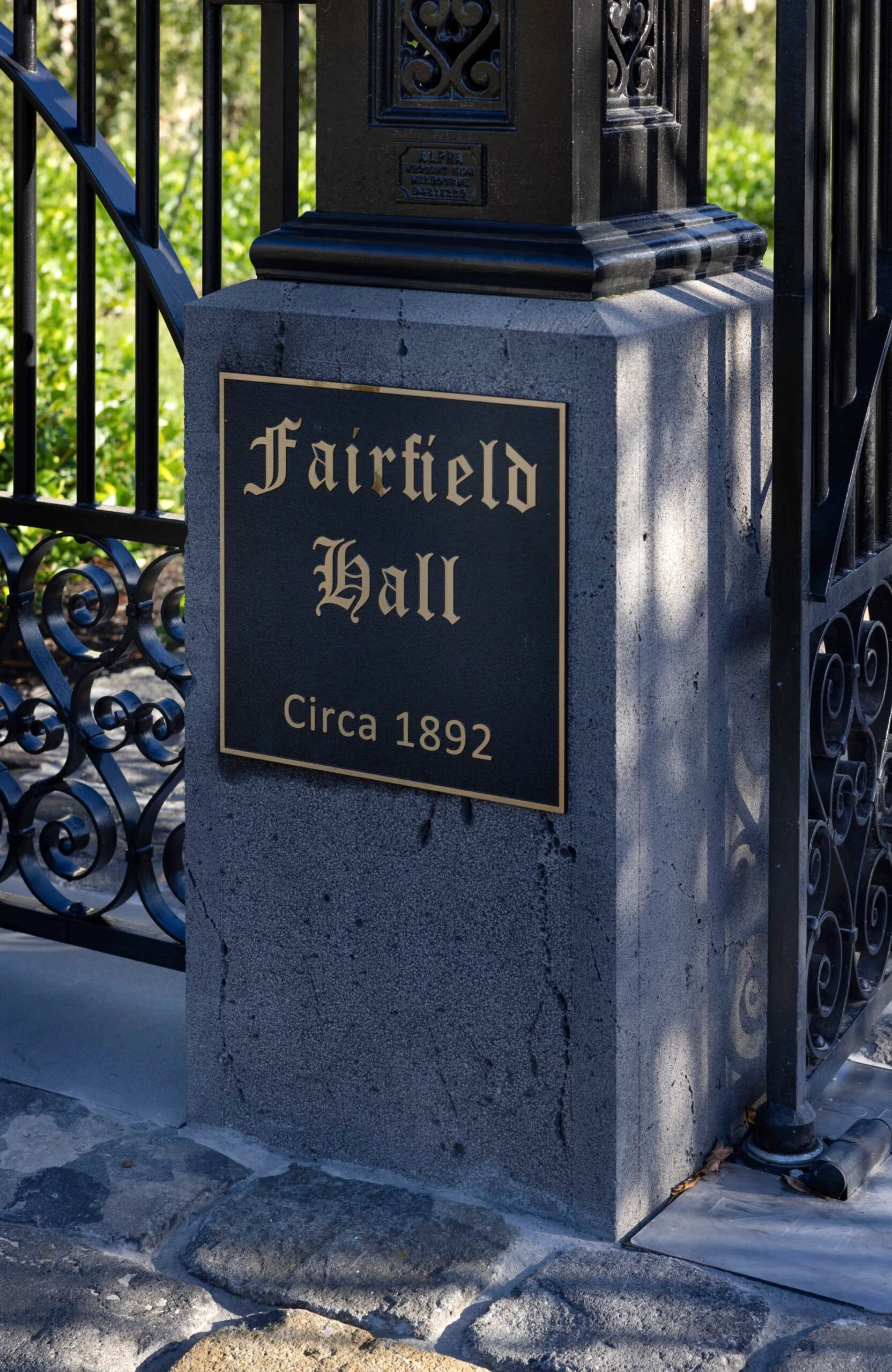 A close up of the pillar of a stone and wrought iron gate, with a sign that read "Fairfield Hall, circa 1892'