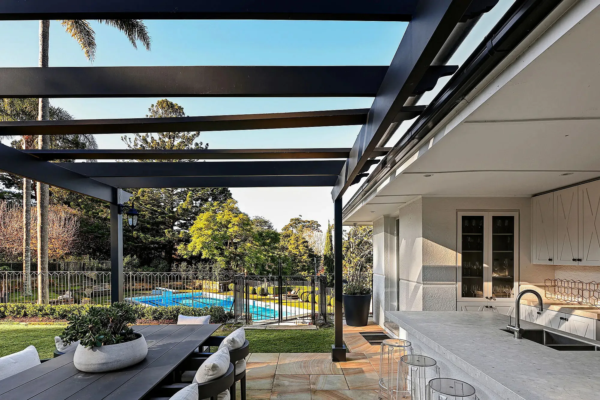 Outdoor kitchen and alfresco dining area with a view of the swimming pool at a Walter Burley Griffin house in Pymble.