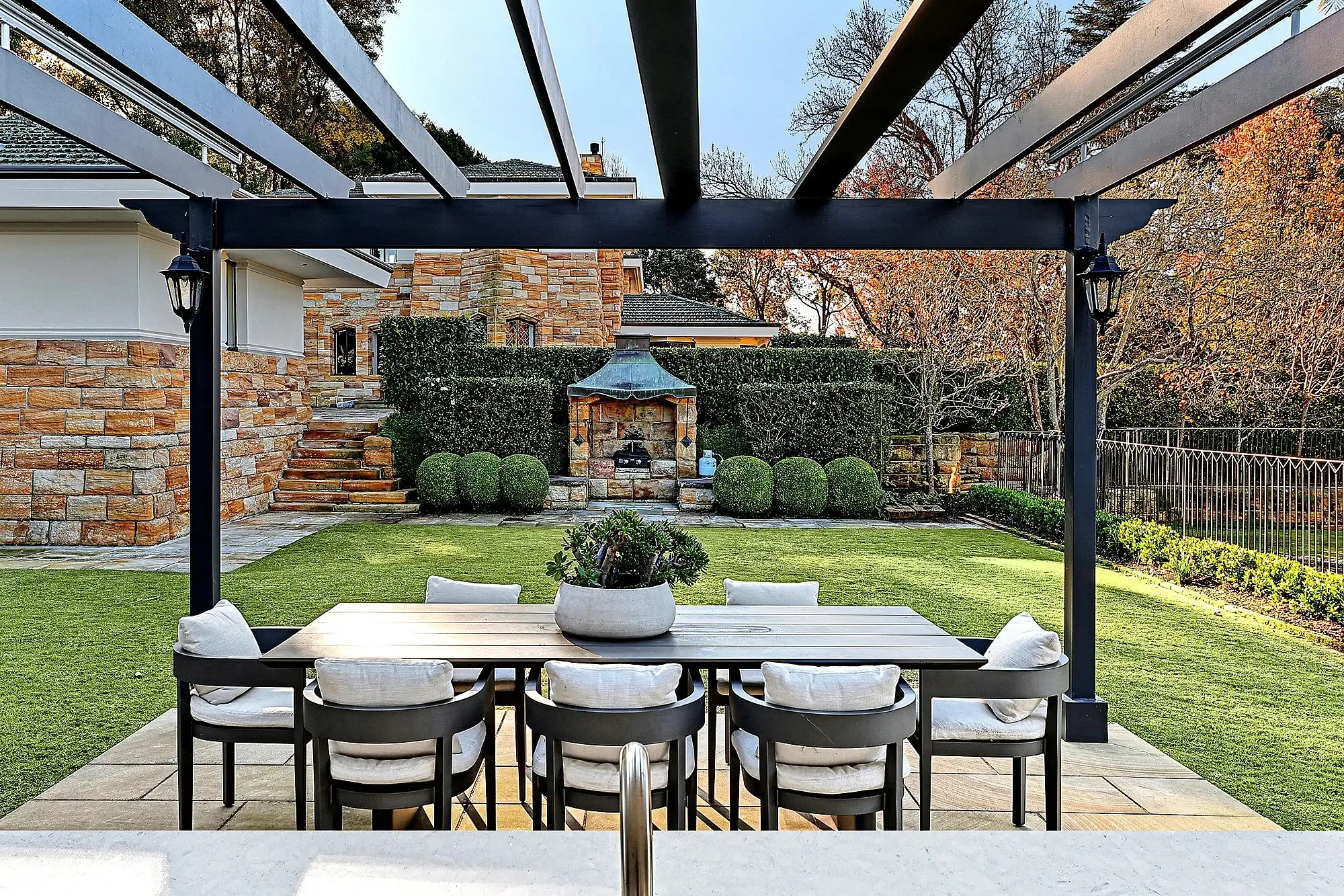 Outdoor dining area in the backyard of a Walter Burley Griffin house in Pymble with a lawn and arbor.
