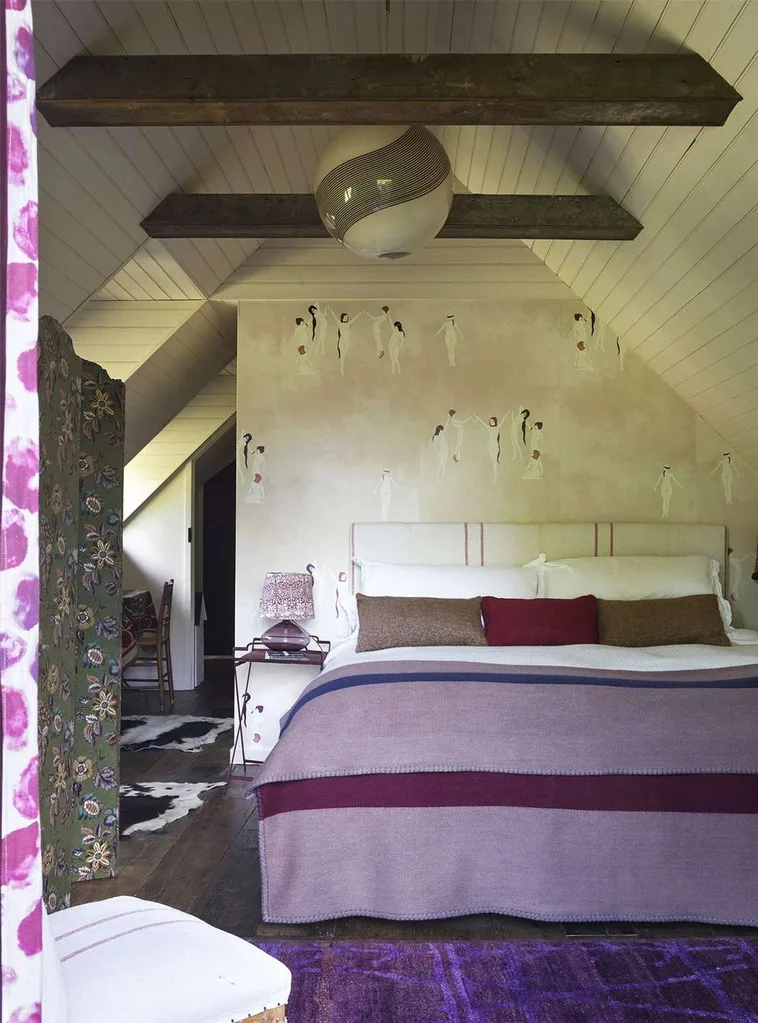 Sienna Miller's bedroom with a purple bedspread and pink wallpaper with figures dancing