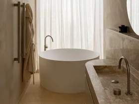 Modern bathroom with a round bathtub, minimalist fixtures, towel rack, and marble countertop beside sheer curtains.