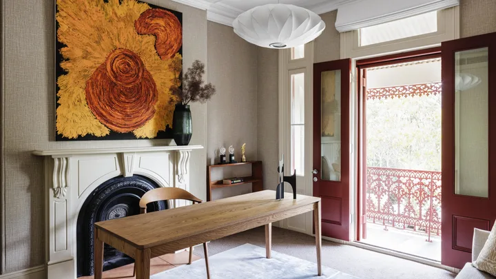 Office with wooden desk, chair, ornate fireplace, abstract painting, and open double doors to a balcony.