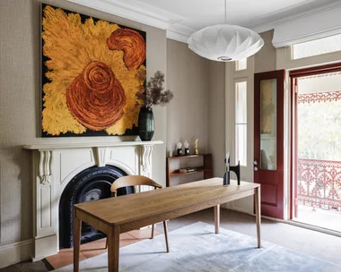 Office with wooden desk, chair, ornate fireplace, abstract painting, and open double doors to a balcony.
