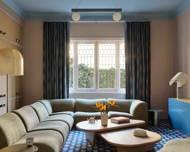 Elegant living room with a curved sofa, geometric carpet, modern lighting, and a window with blue curtains.