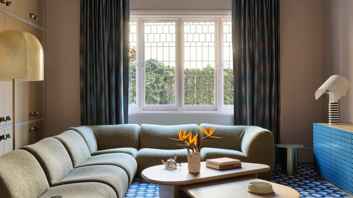 Elegant living room with a curved sofa, geometric carpet, modern lighting, and a window with blue curtains.
