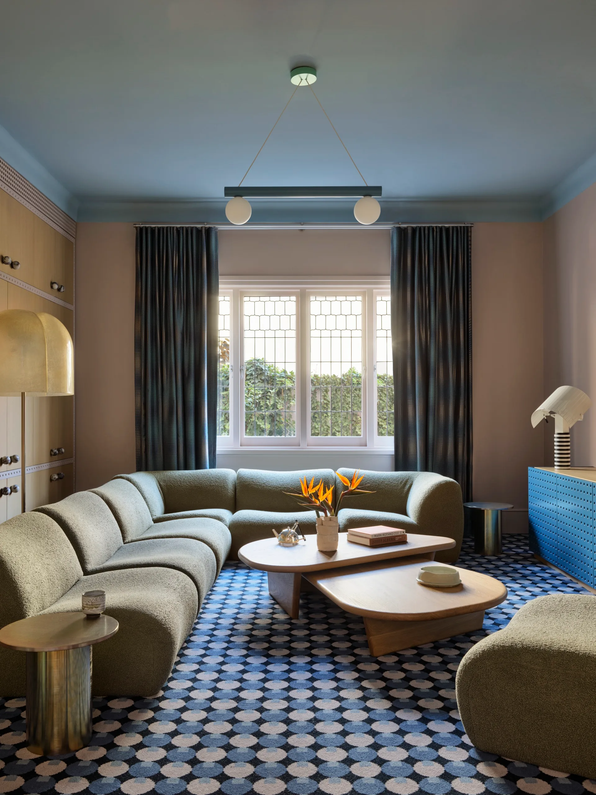 Elegant living room with a curved sofa, geometric carpet, modern lighting, and a window with blue curtains.