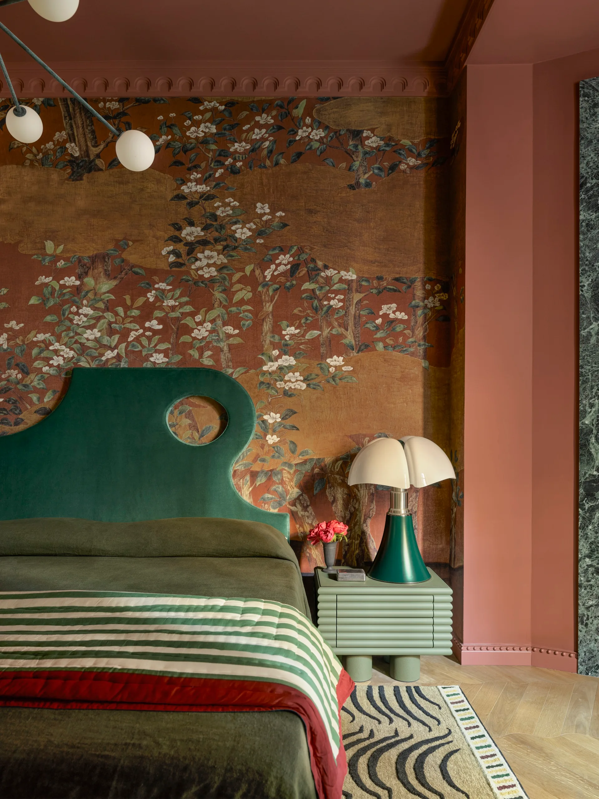 Bedroom with floral wallpaper, green headboard, striped bedding, and a unique lamp on a nightstand.