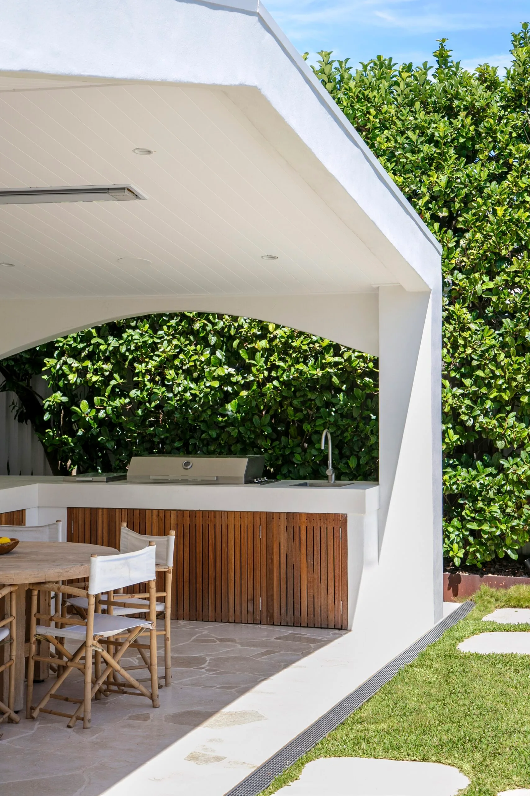 Covered outdoor kitchen and barbecue with outdoor furniture and crazy pavers in a well-landscaped backyard.