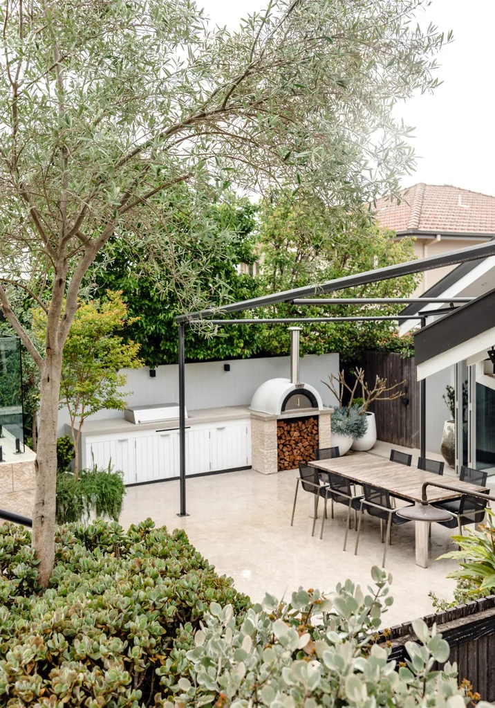 An outdoor kitchen and dining area with a barbecue, and under bench cabinetry. Greenery surrounds this alfresco area.