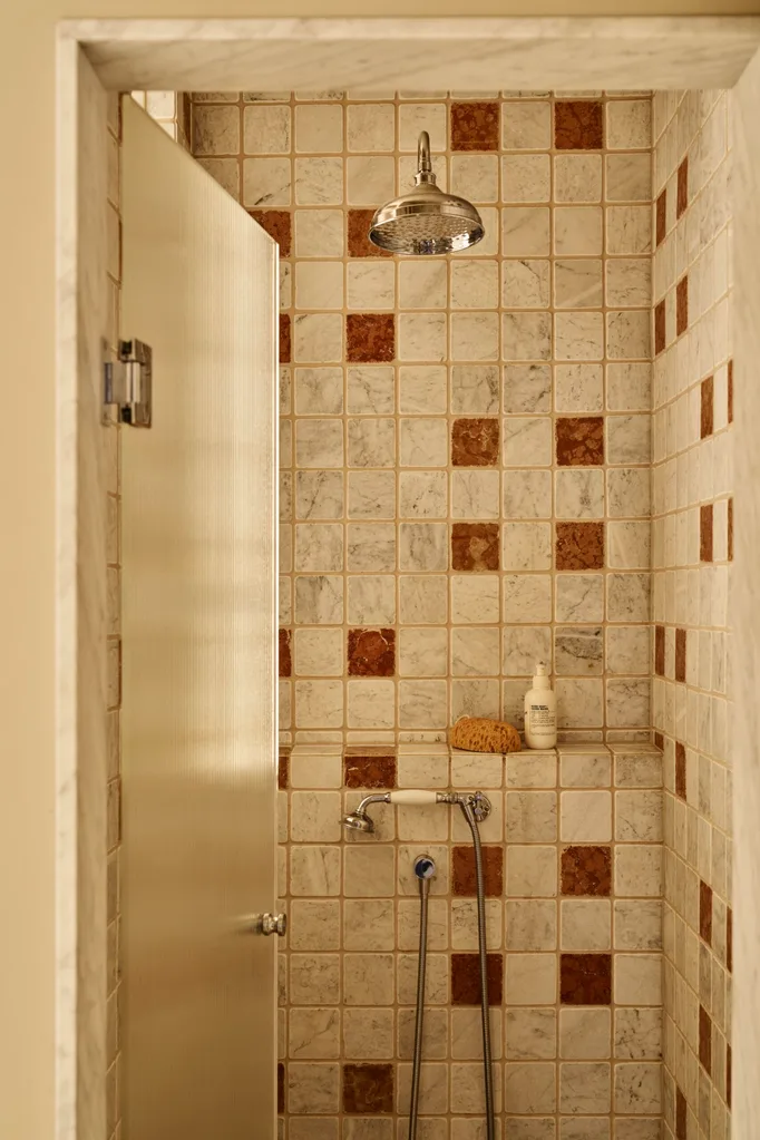 Walk-in shower with white and brown tiles, featuring a nickel showerhead and tapware, a built-in ledge with a sponge and product atop.