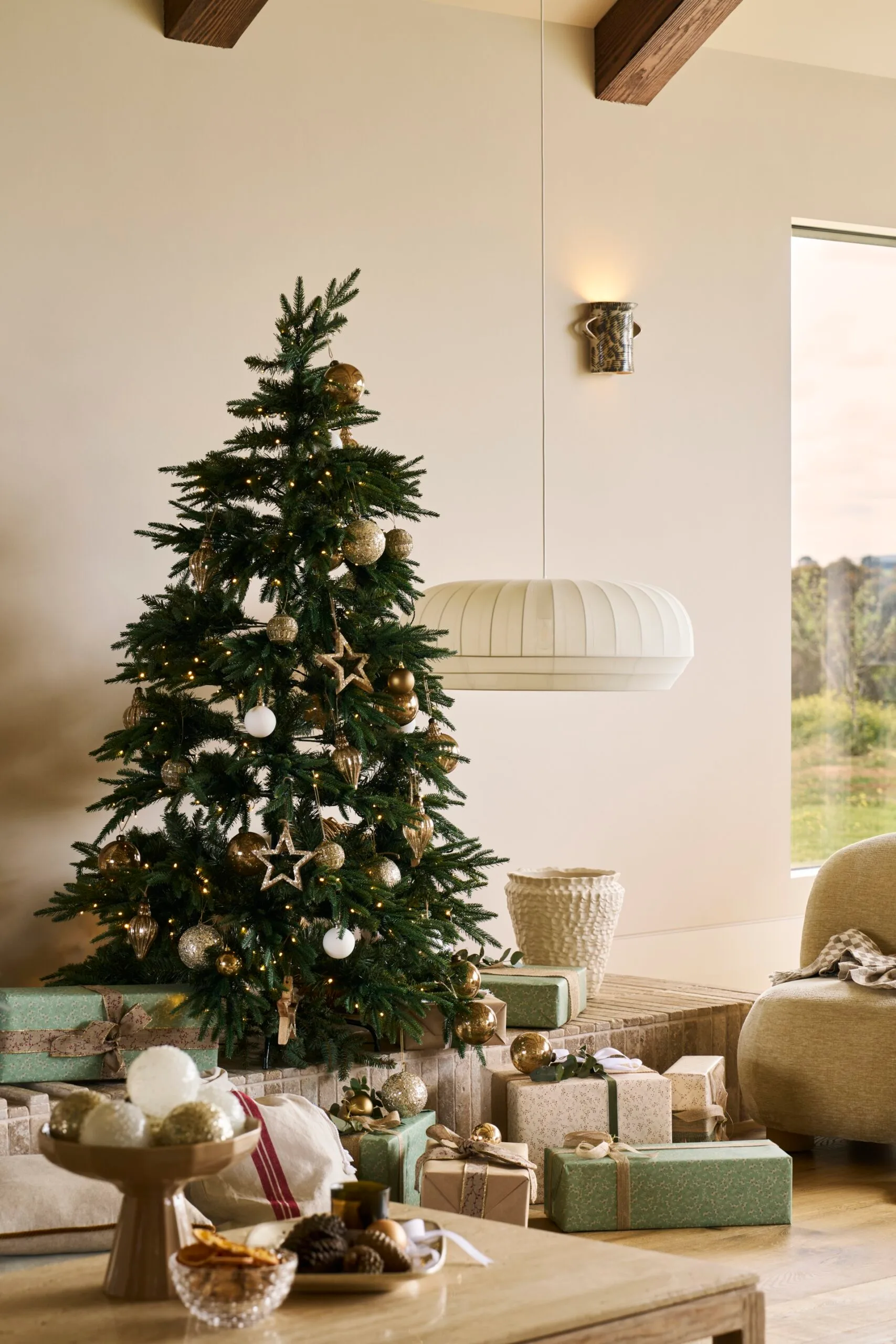 Decorated Christmas tree with gold and white ornaments, surrounded by wrapped Christmas presents in a cosy living room setting.