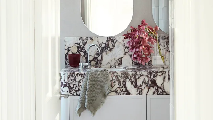 A bathroom with a marble sink, oval mirrors, pink flowers, and a gray towel hanging on the counter.