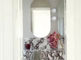 A bathroom with a marble sink, oval mirrors, pink flowers, and a gray towel hanging on the counter.