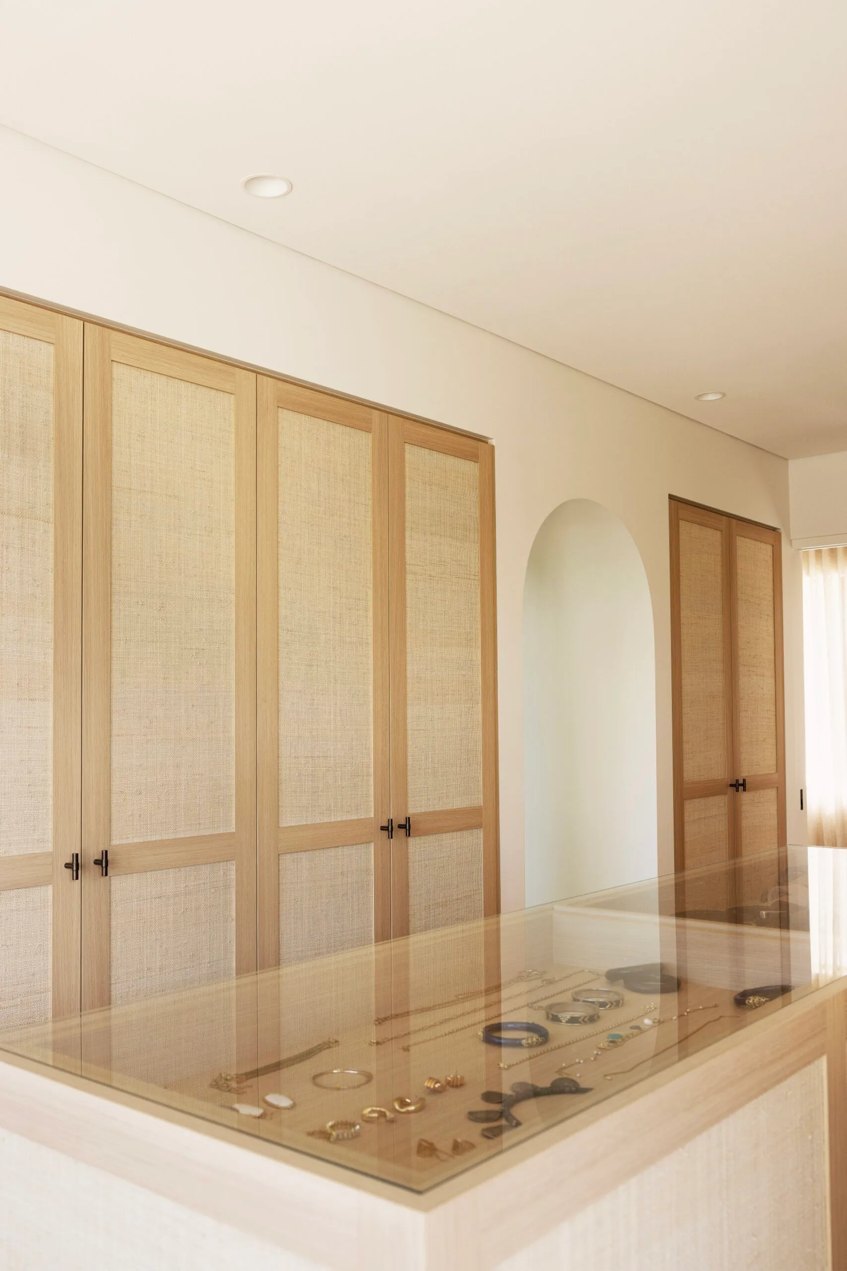 Walk-in robe in a coastal Sydney Mediterranean-style house featuring rattan cupboard doors and a jewellery display cabinet.