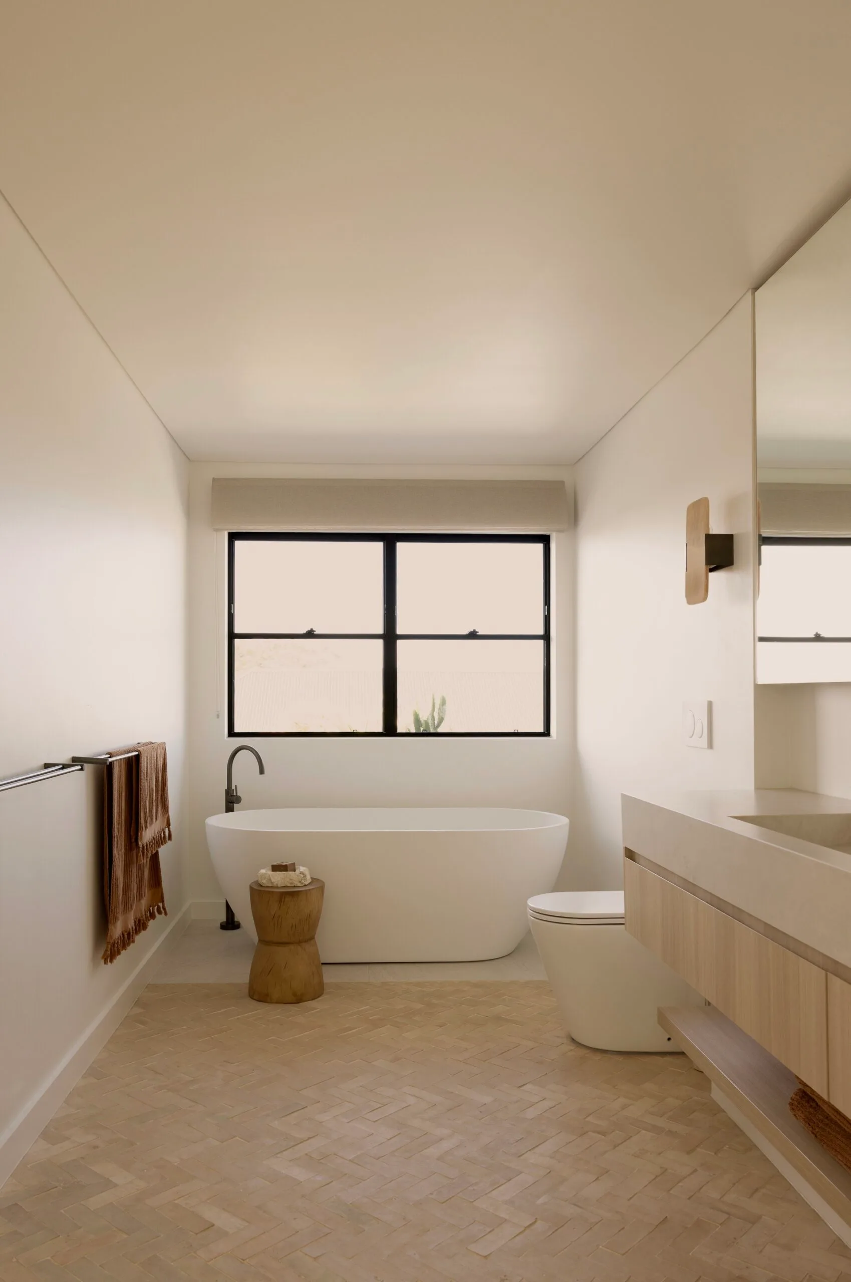 Main ensuite bathroom in a coastal Sydney house with a neutral, beige Mediterranean aesthetic featuring ABI Interiors freestanding bathtub and natural clay floor tiles.