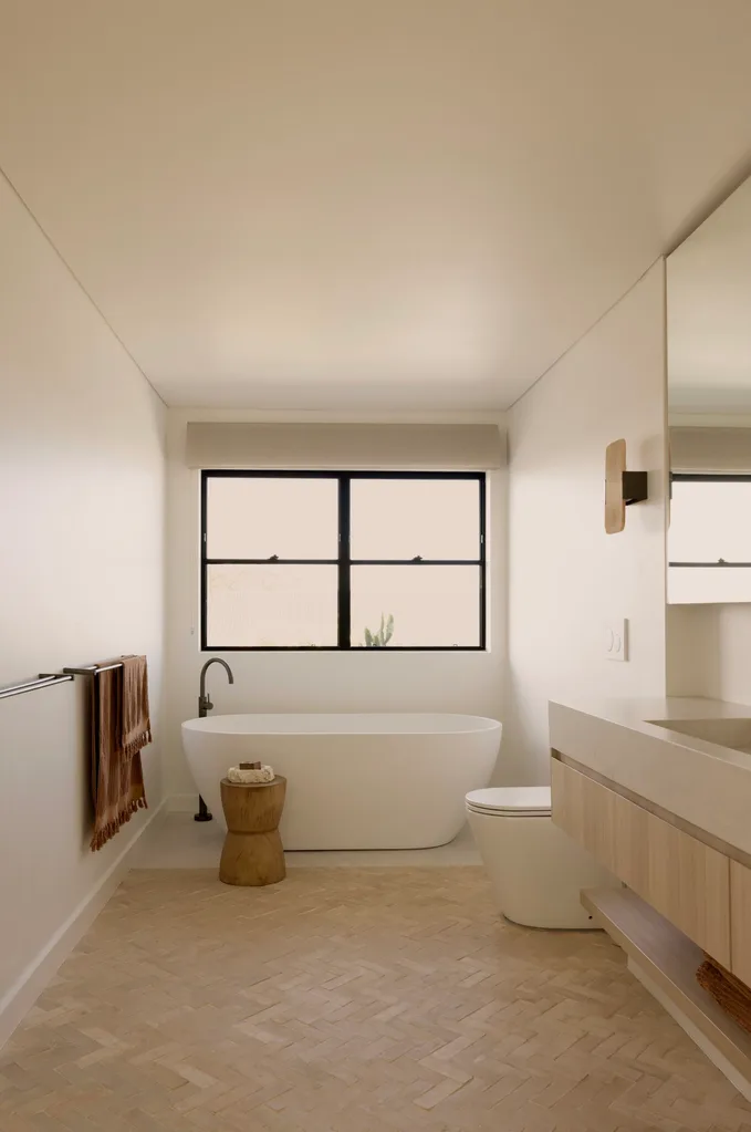 Main ensuite bathroom in a coastal Sydney house with a neutral, beige Mediterranean aesthetic featuring ABI Interiors freestanding bathtub and natural clay floor tiles.