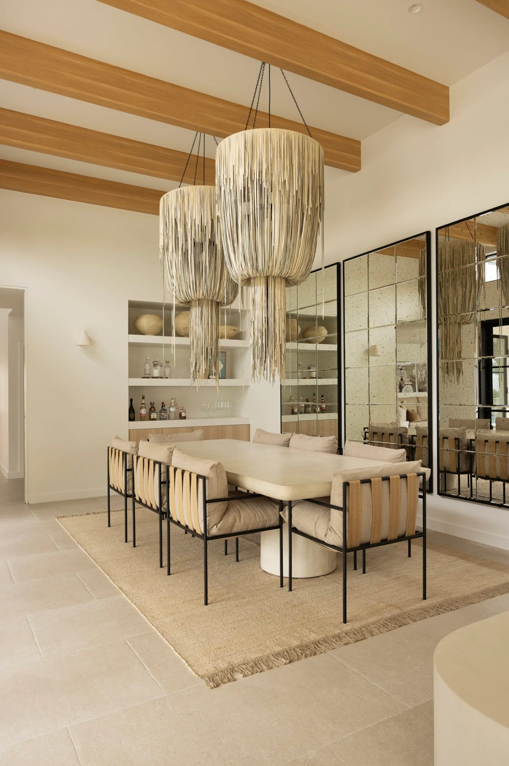Formal dining room in a coastal Sydney house with a neutral, beige Mediterranean aesthetic featuring leather Balinese pendant lights and rustic mirrors.