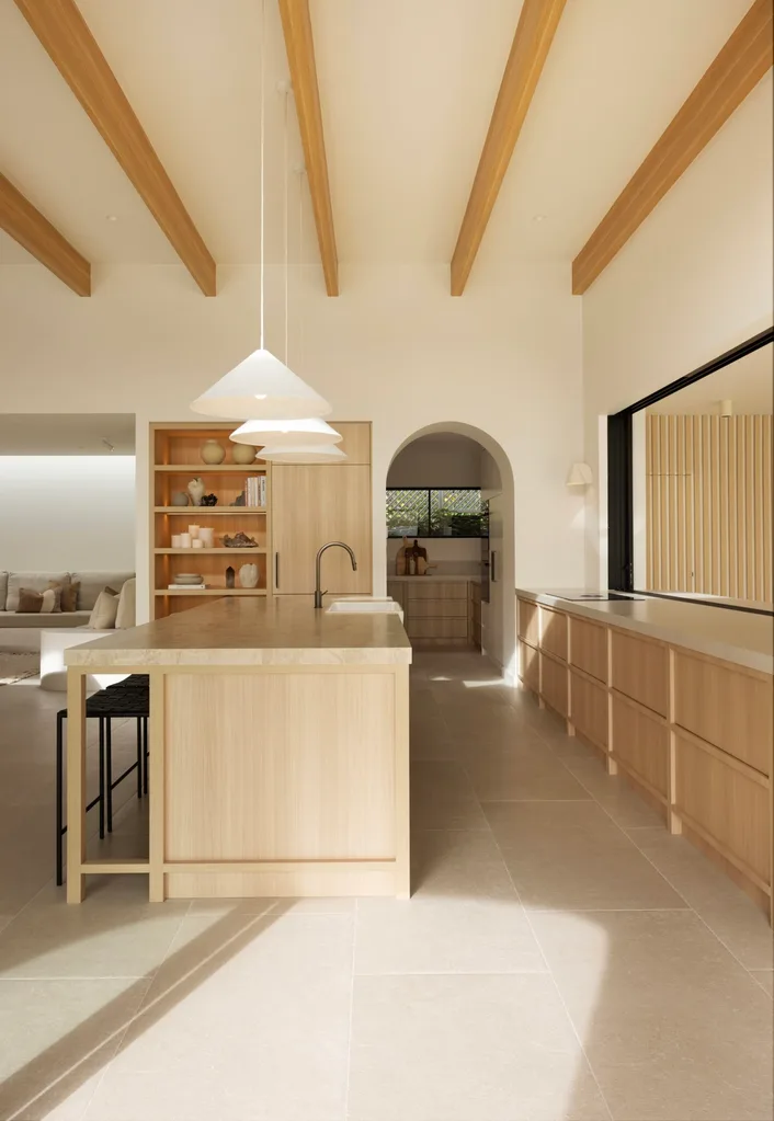 Kitchen in a Sydney coastal house with a neutral Mediterranean aesthetic featuring a stone kitchen island bench and exposed ceiling beams.