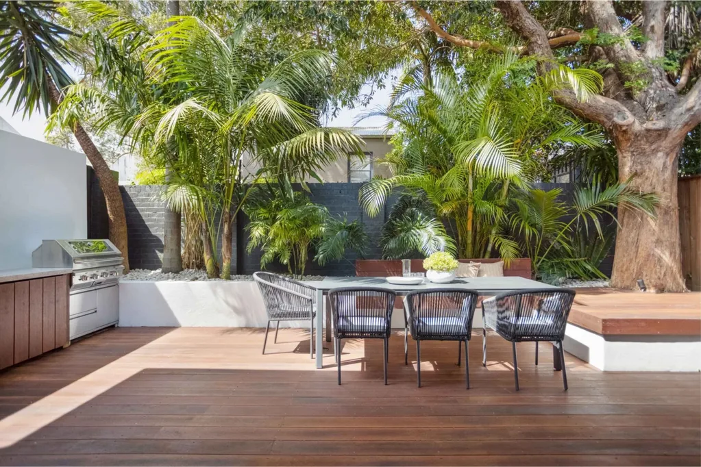 Backyard timber deck and barbecue area with a tropical garden and outdoor dining table and chairs.