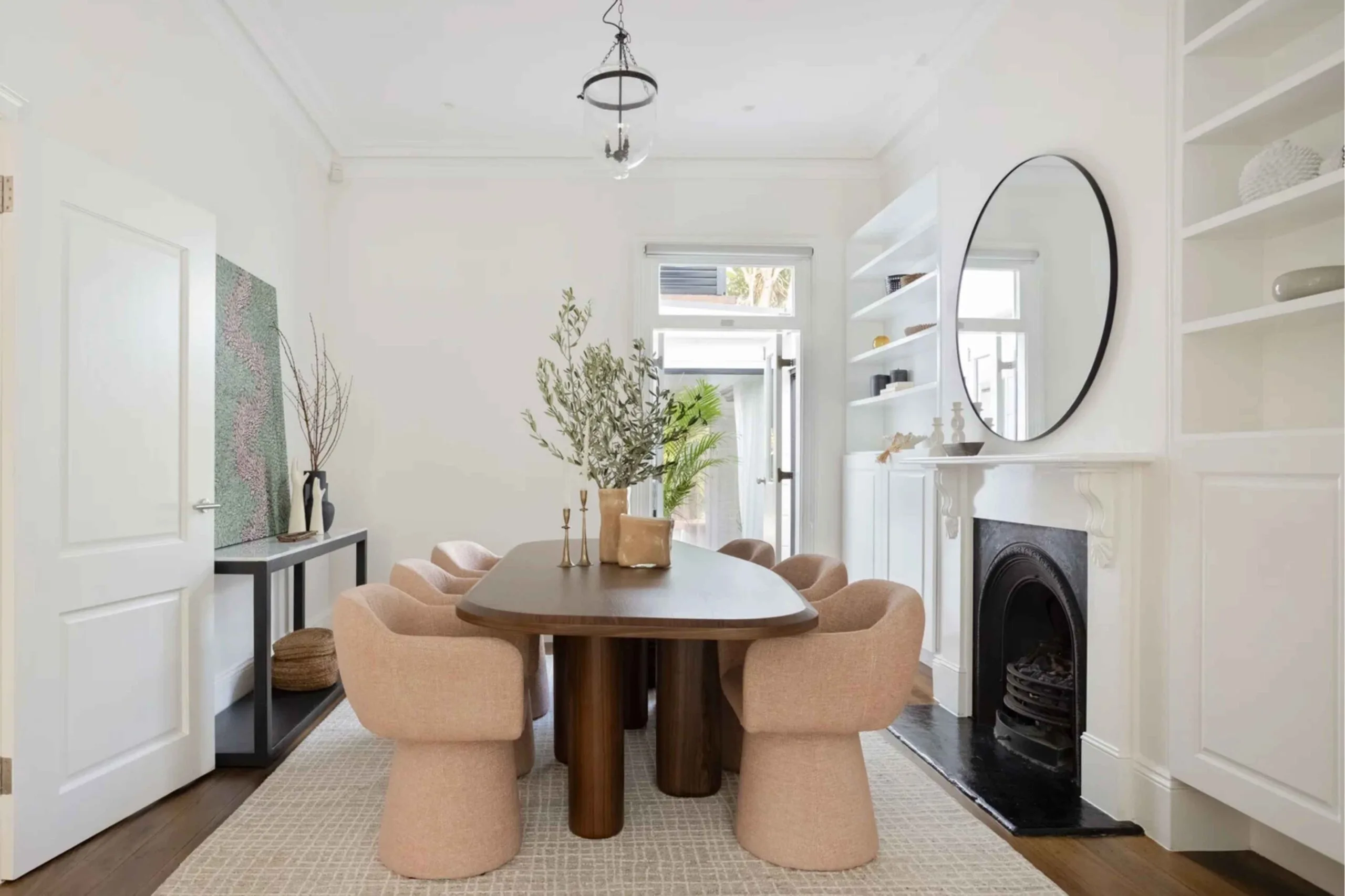 White formal dining room with a fireplace in a Victorian terrace-style house, featuring a timber dining table and blush-pink dining chairs.