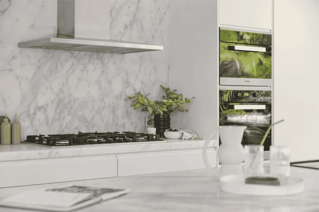 Close-up view of a marble kitchen splashback, stovetop and rangehood, with marble kitchen island bench in foreground.
