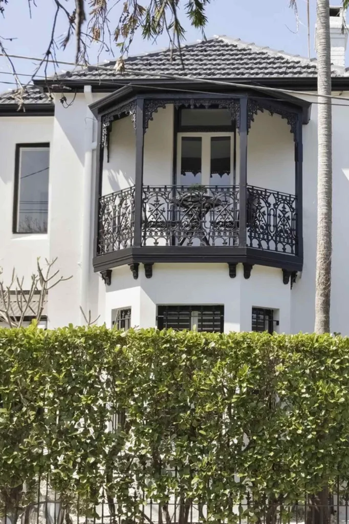 Front of a white Victorian terrace-style house with black fretwork and a garden hedge.
