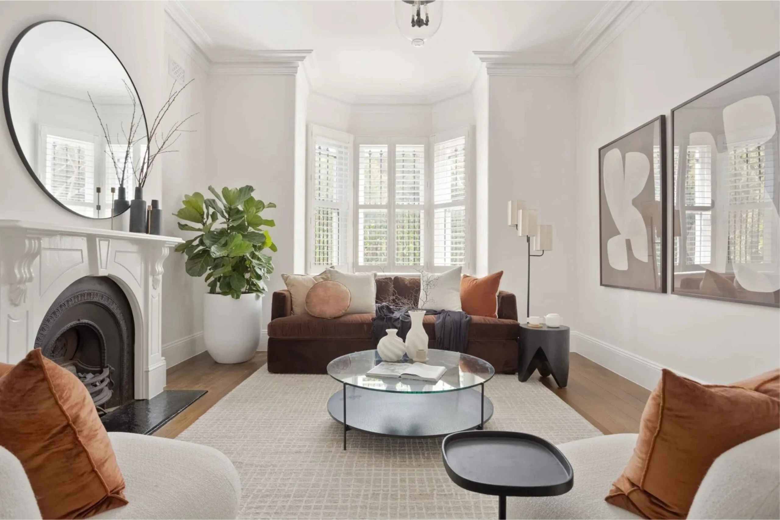 White formal living room with a bay window in a Victorian terrace-style house, featuring brown and rust-coloured furniture and decor.