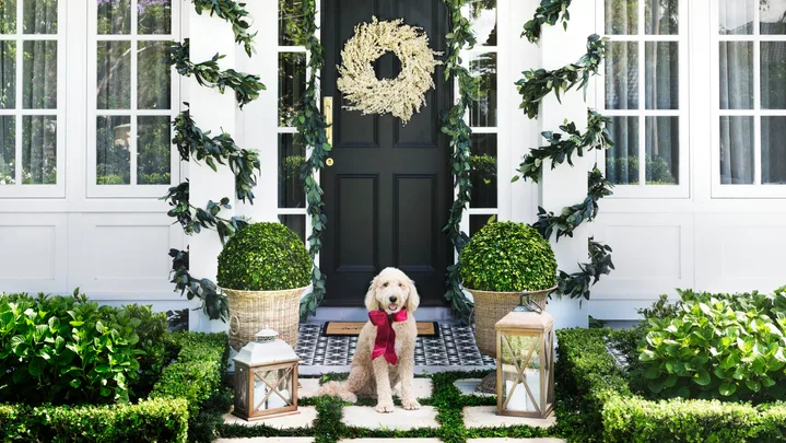 White home exterior with white berry Christmas wreath on the front door and eucalyptus garlands wrapped around portico collumns