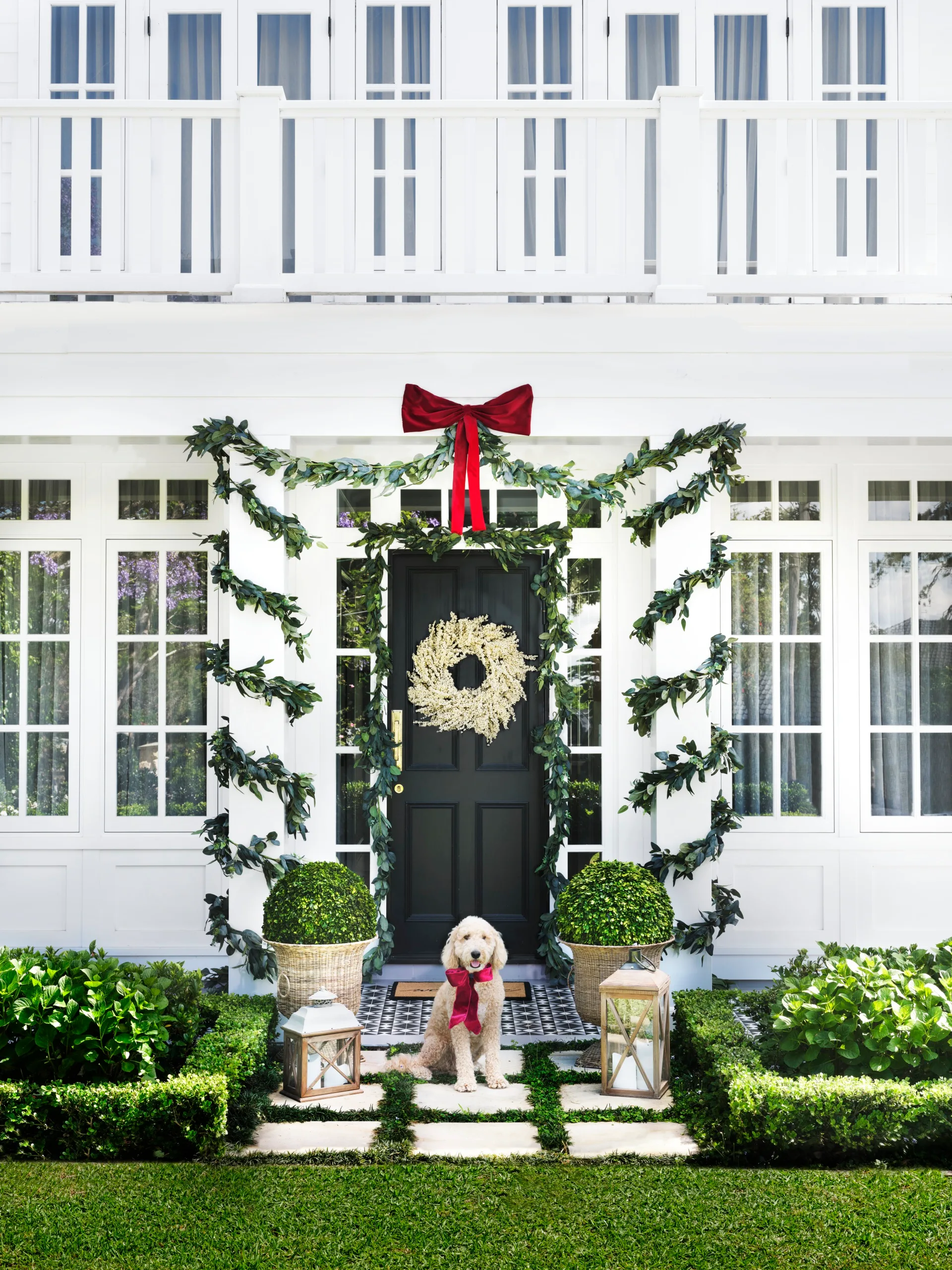 White home exterior with white berry Christmas wreath on the front door and eucalyptus garlands wrapped around portico collumns
