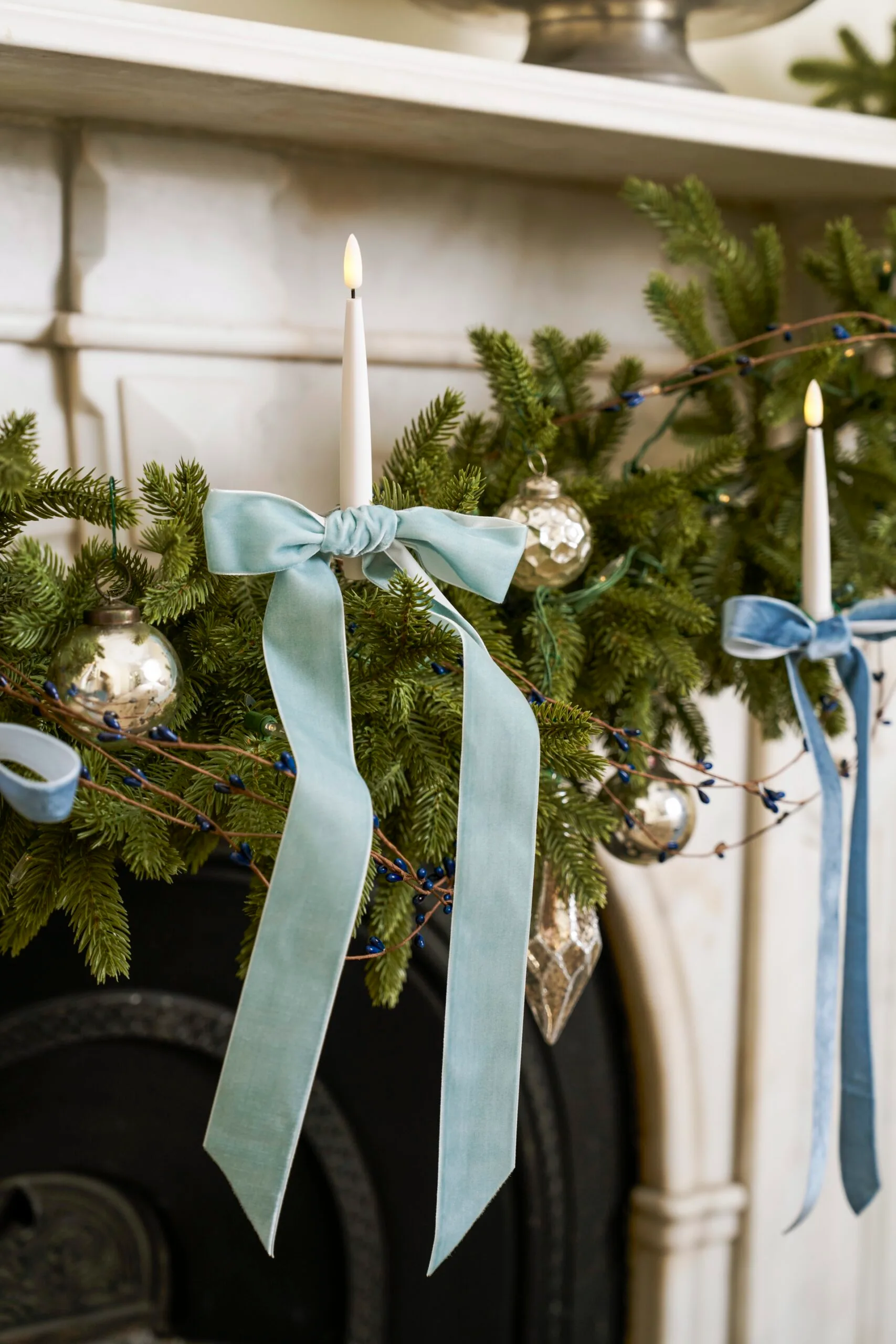 Christmas bows and candles decorate a mantle piece. 