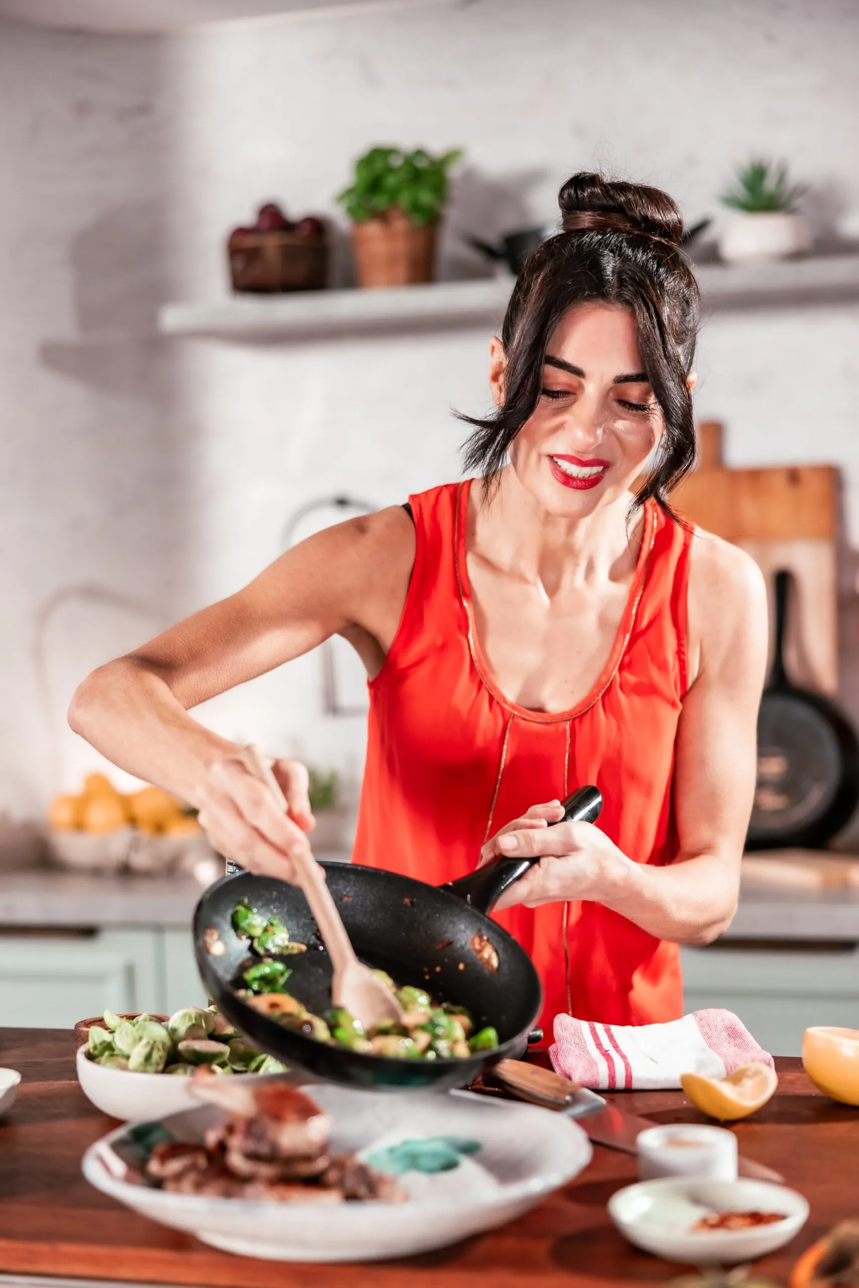 Silvia Colloca wears a red shirt and spoons brussel sprouts out of a saucepan and on to a plate