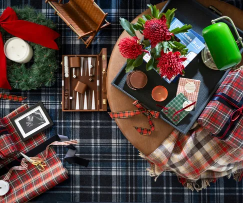 Birds-eye view of an ottoman and tartan rug styled like a tablescape with festive decor, gifts and homewares.