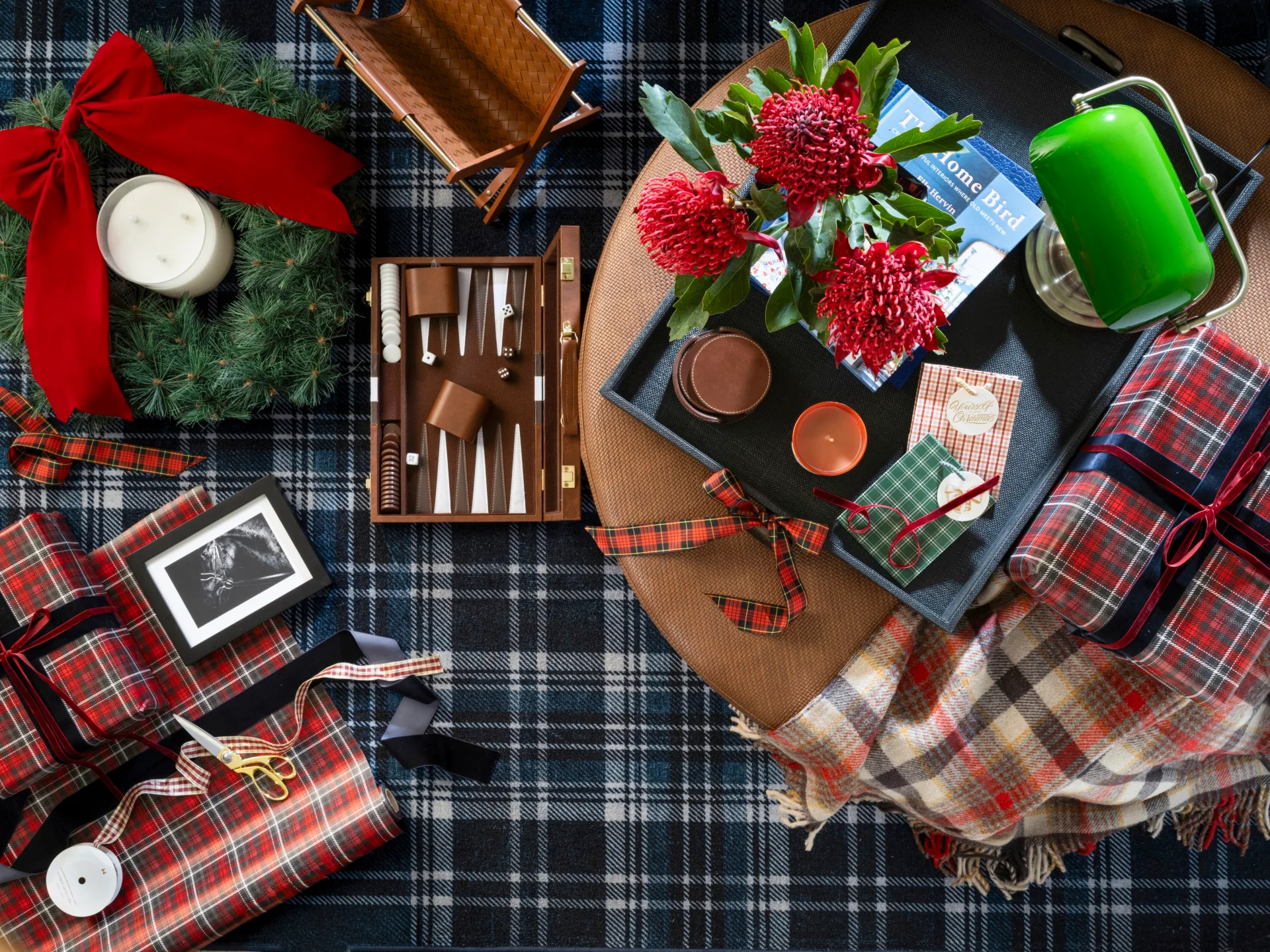 Festive ottoman decorated with gifts, homewares, giftwrapping, tartan, a lamp and red accents.