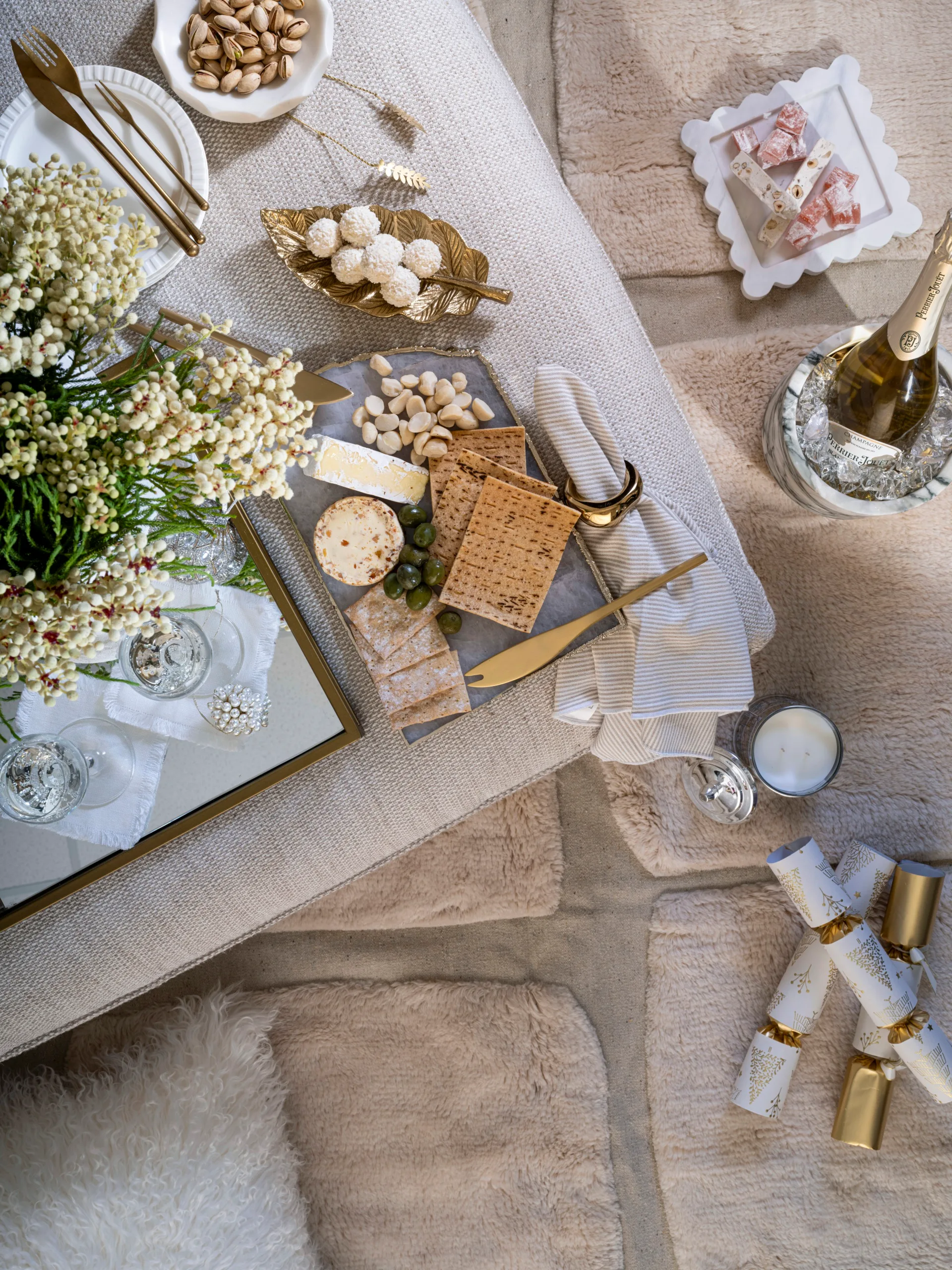 A festive ottoman decorated and styled in a classic, beige and neutral theme with champagne, a cheese platter and bonbons.