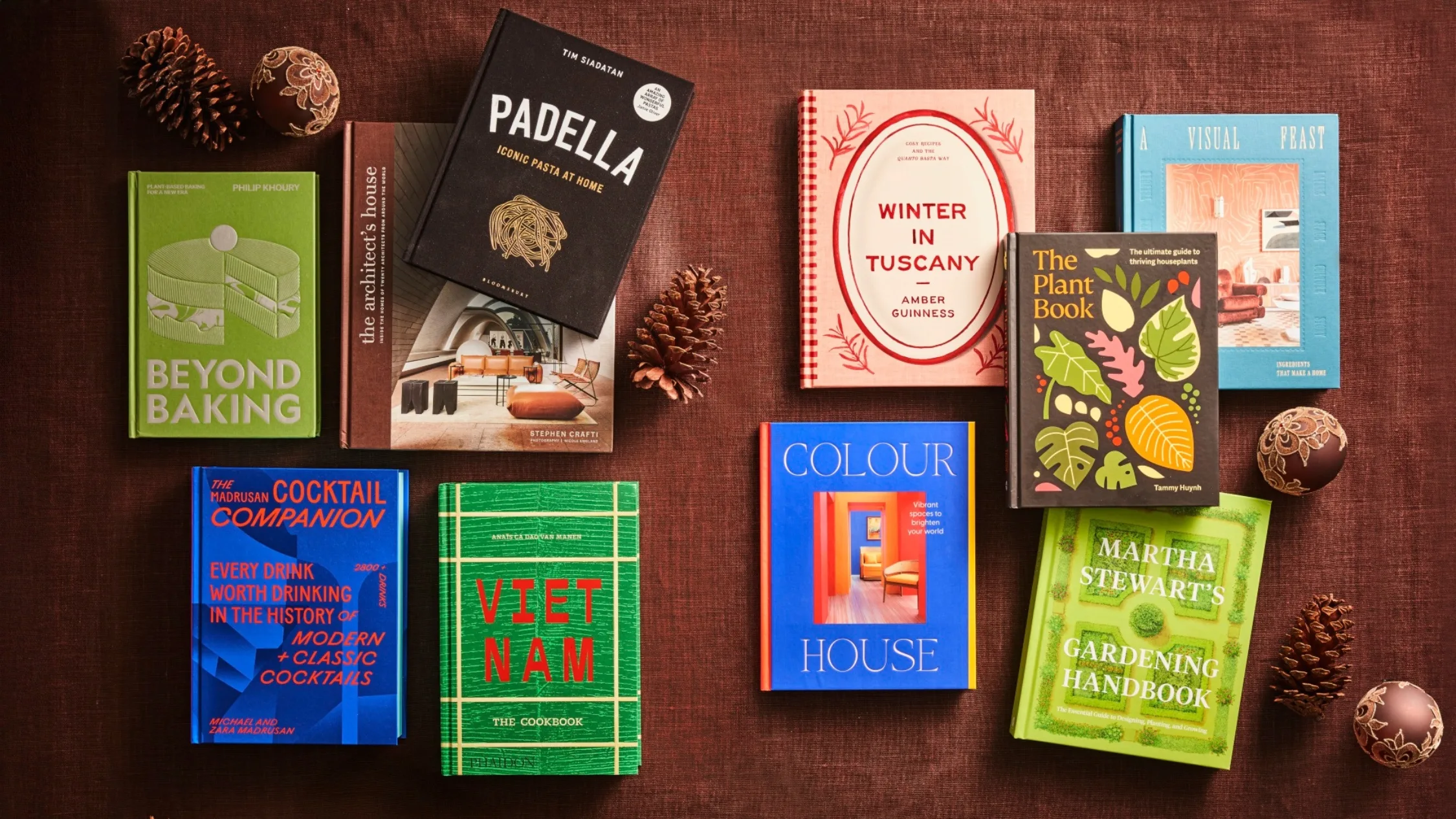 the latest interior design, gardening and cook books arranged on brown velvet fabric with pine cones and Christmas baubles