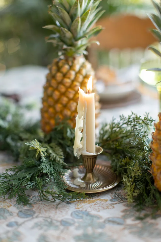 Tara Dennis River House Christmas Entertaining pineapple themed dining table decorations with a lit tapered candle melting down to a brass candlestick
