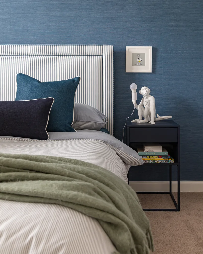 Bed with blue-striped headboard, green blanket, blue pillows, and a monkey lamp on a black nightstand with books.