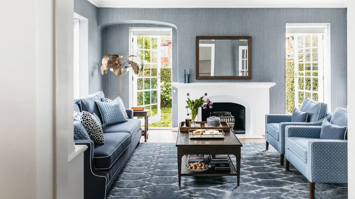 Cozy living room with blue sofa, armchairs, fireplace, coffee table, large mirror, and open French doors to garden.