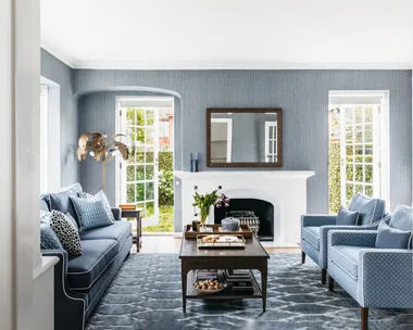 Cozy living room with blue sofa, armchairs, fireplace, coffee table, large mirror, and open French doors to garden.