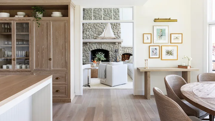 Cozy living room with stone fireplace, white sofas, wooden dining table, and framed artwork on cream walls.